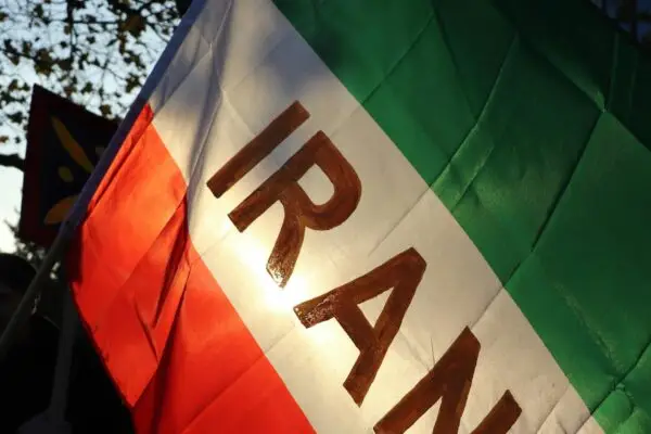 Patriotic display of the Iranian flag waving outdoors against a backdrop of trees.